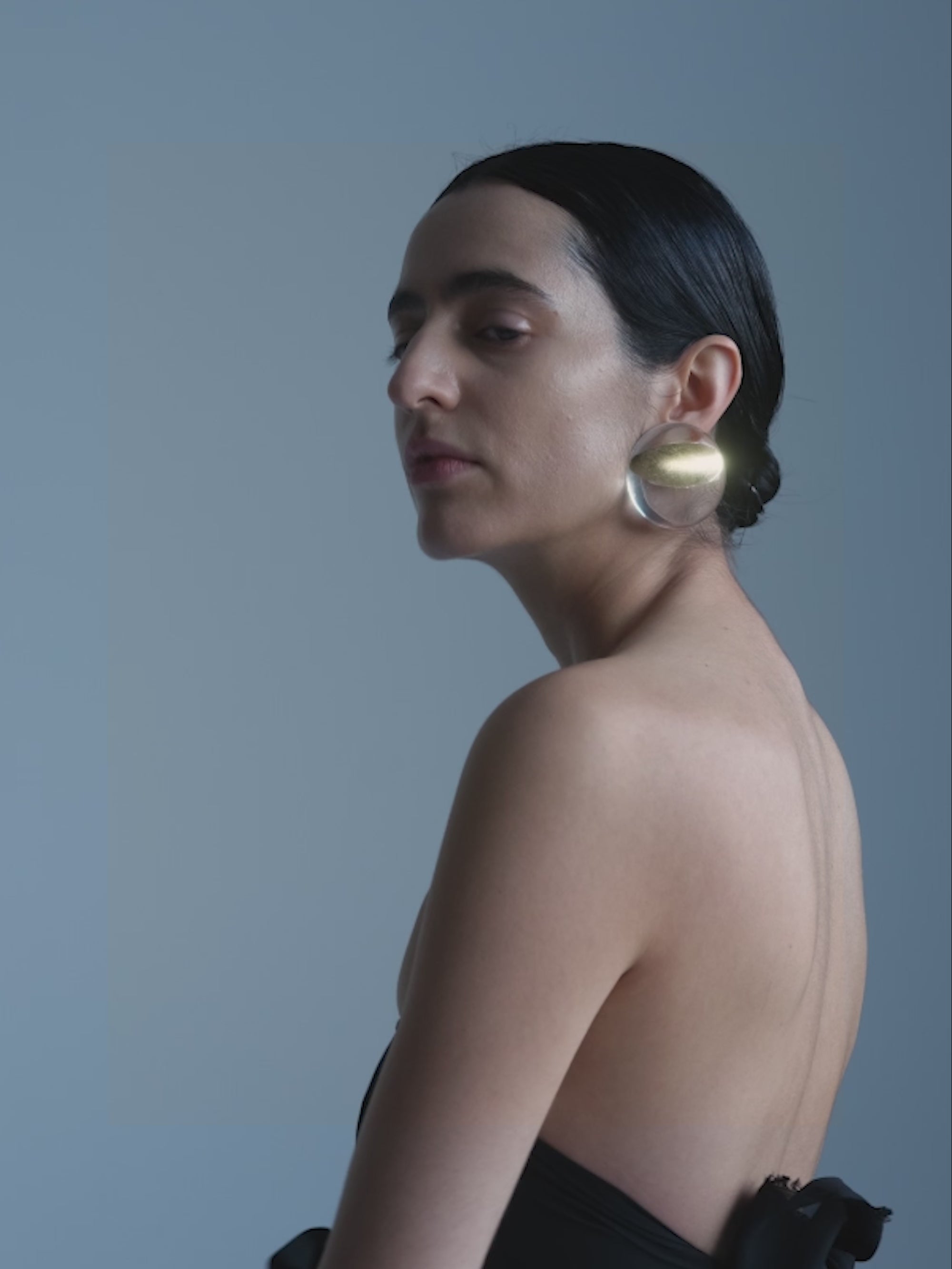 women wearing big gold and transparent earrings against a plain background