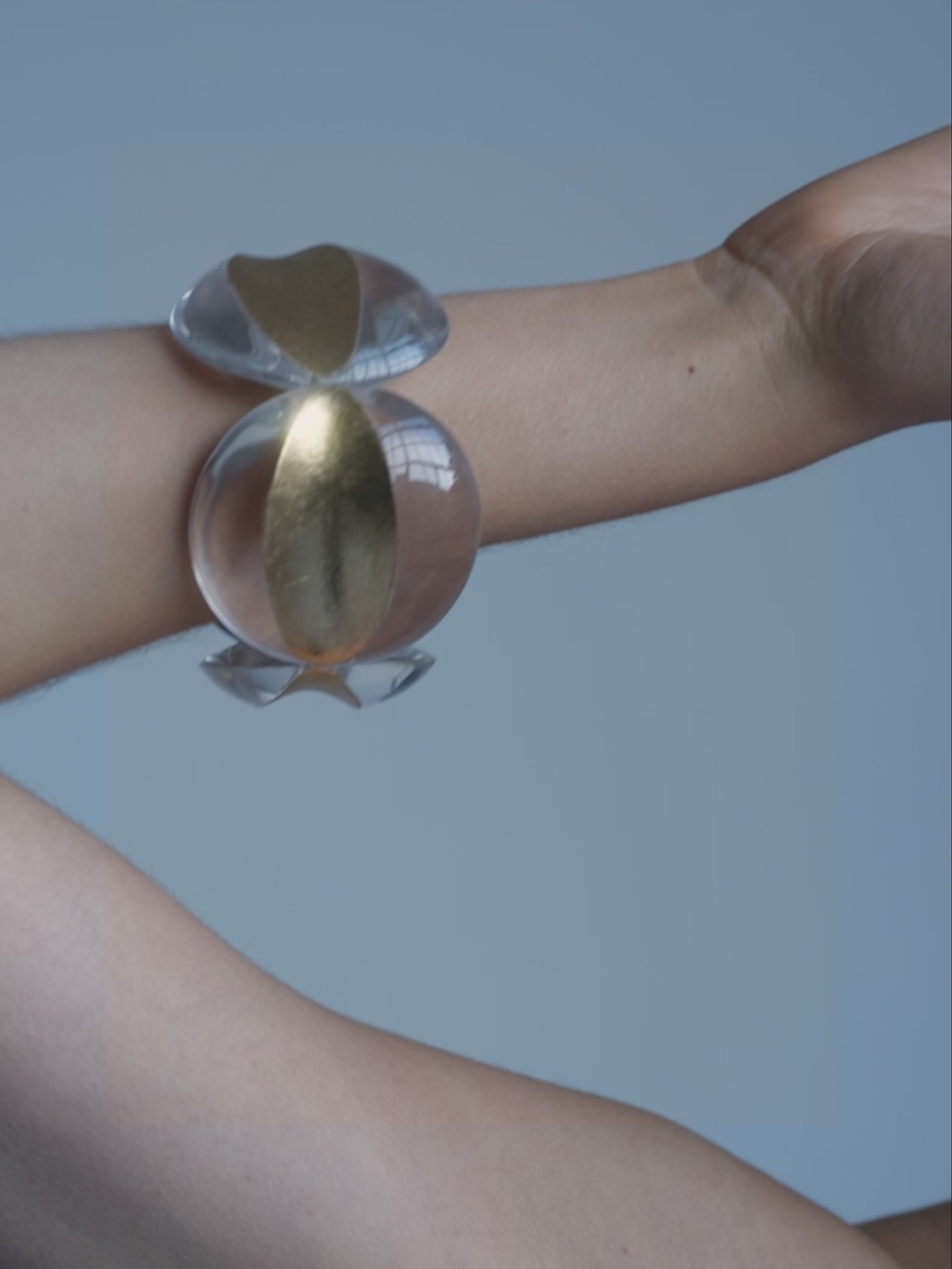 Woman wearing  a transparent bracelet with gold foil details against a white background