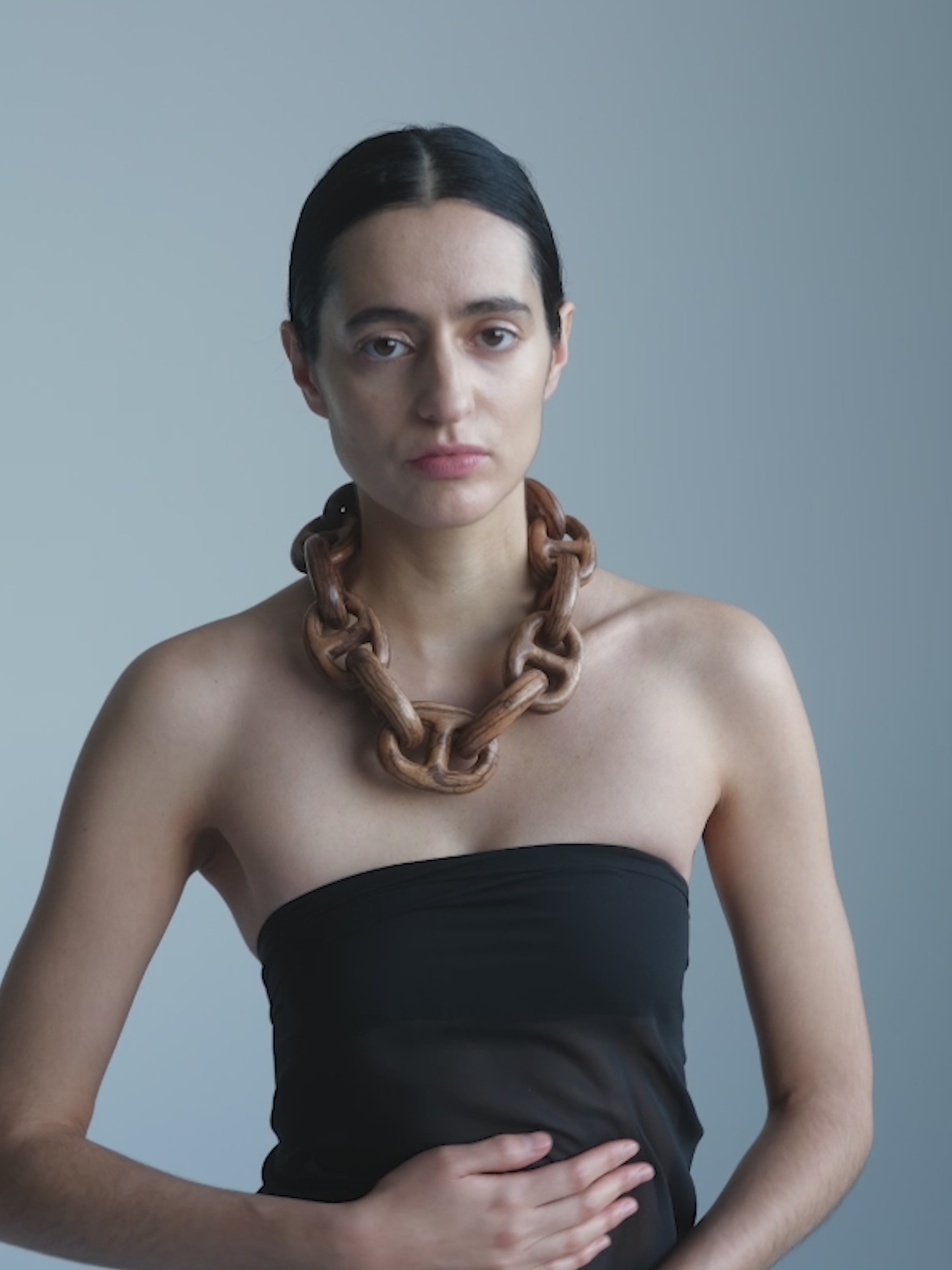 Woman wearing a large, wooden necklace against a plain background