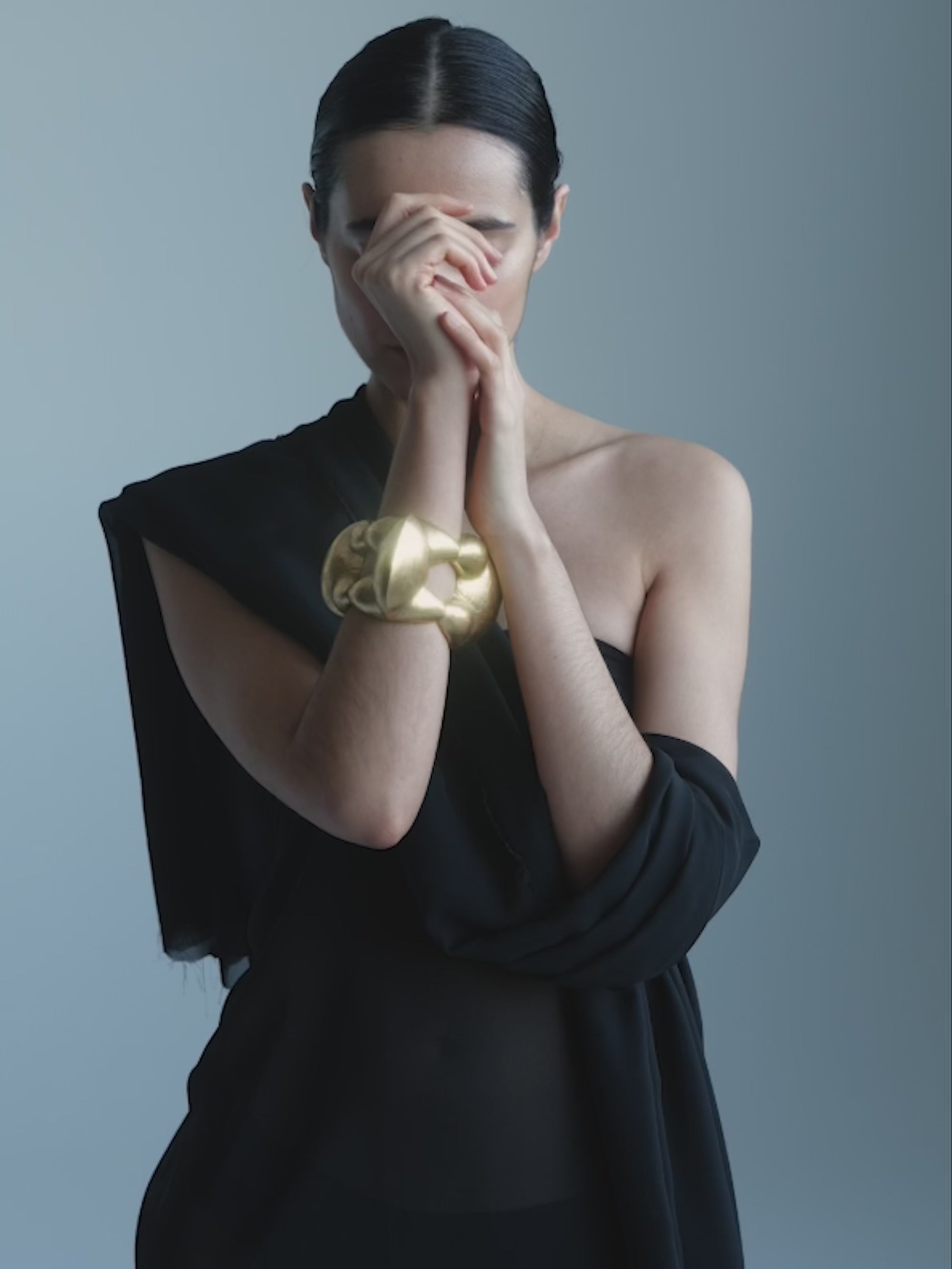 Woman with a gold bracelet on her wrist against a gray background