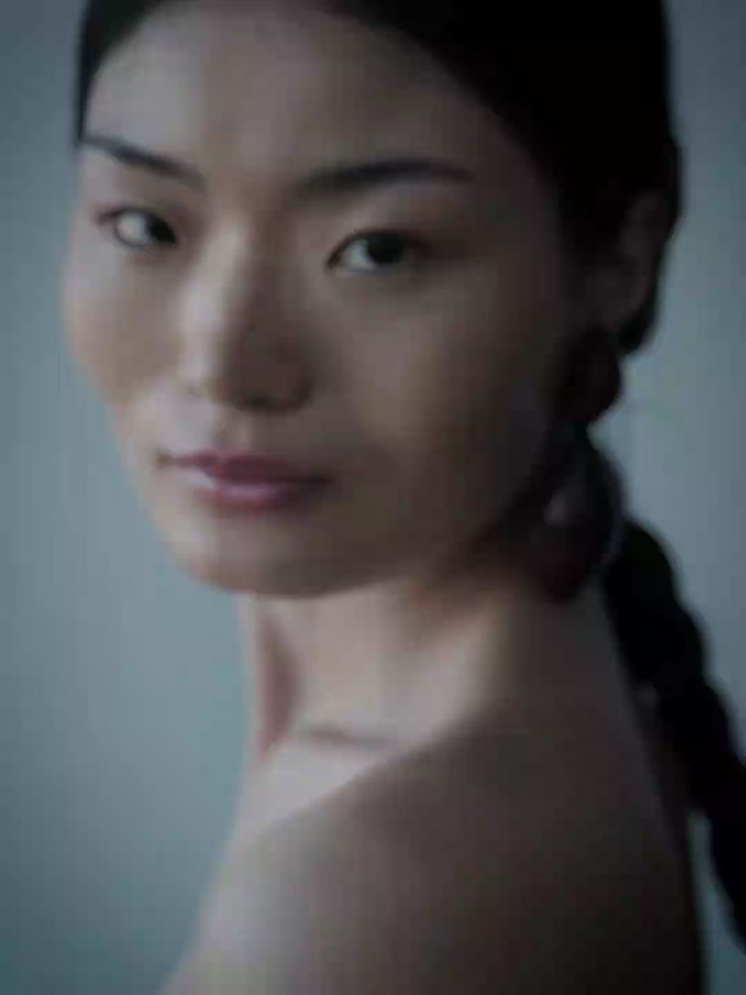 A close-up side profile of a woman wearing a large dark teardrop earring against a muted blue-gray background.