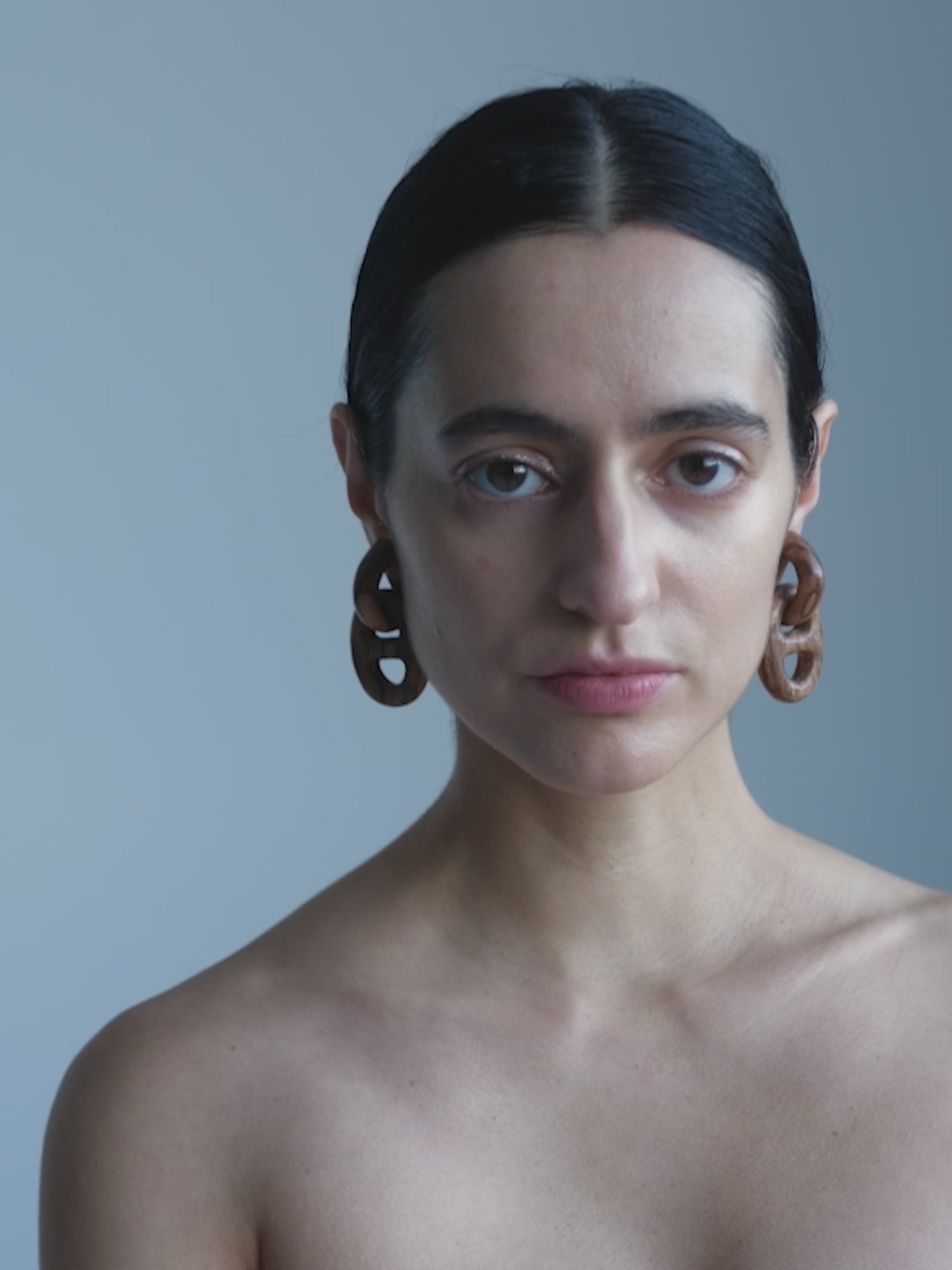Woman with dark hair and earrings against a plain background