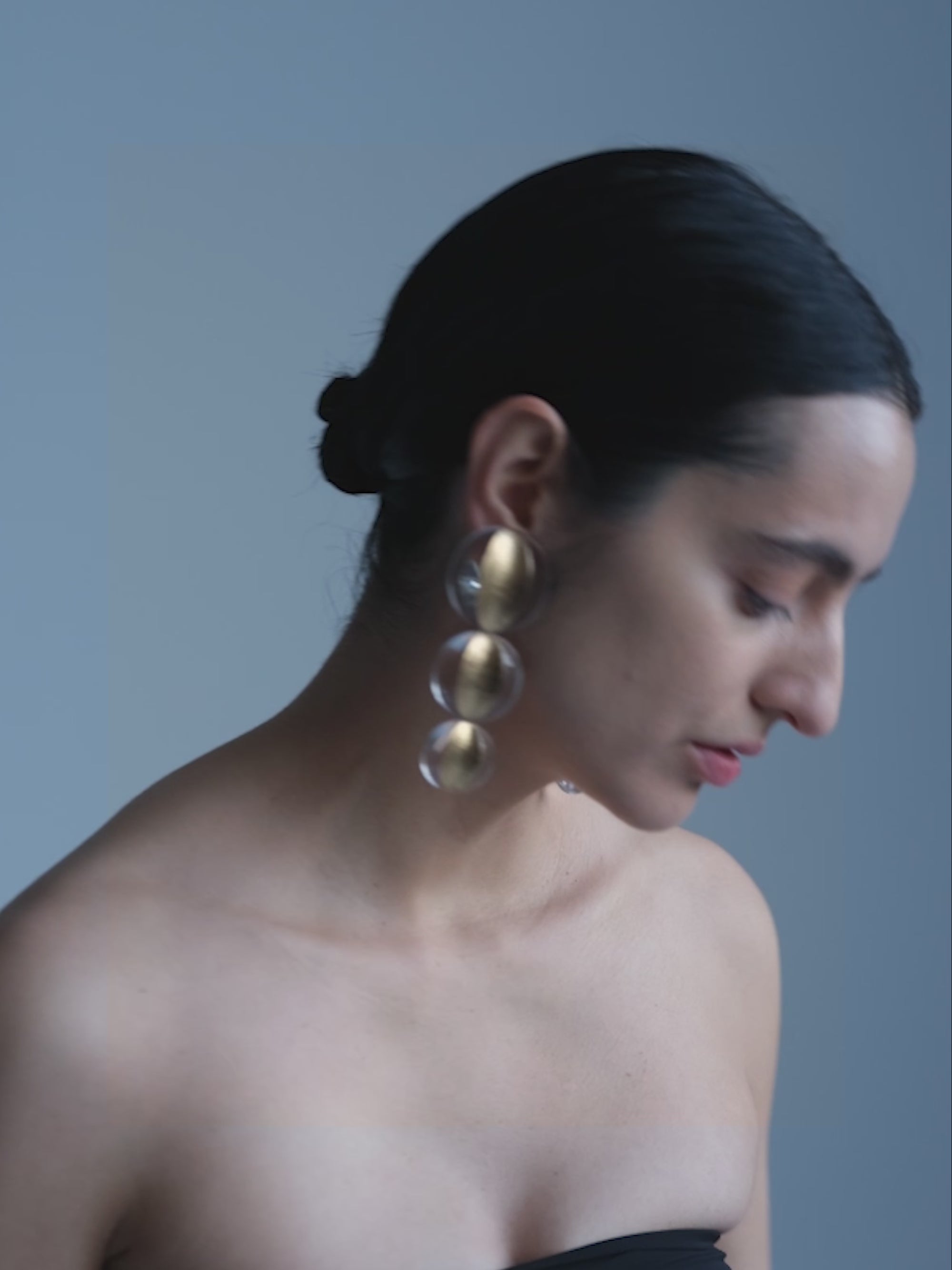 woman wearing a pair of gold and transparent earrings on a white background