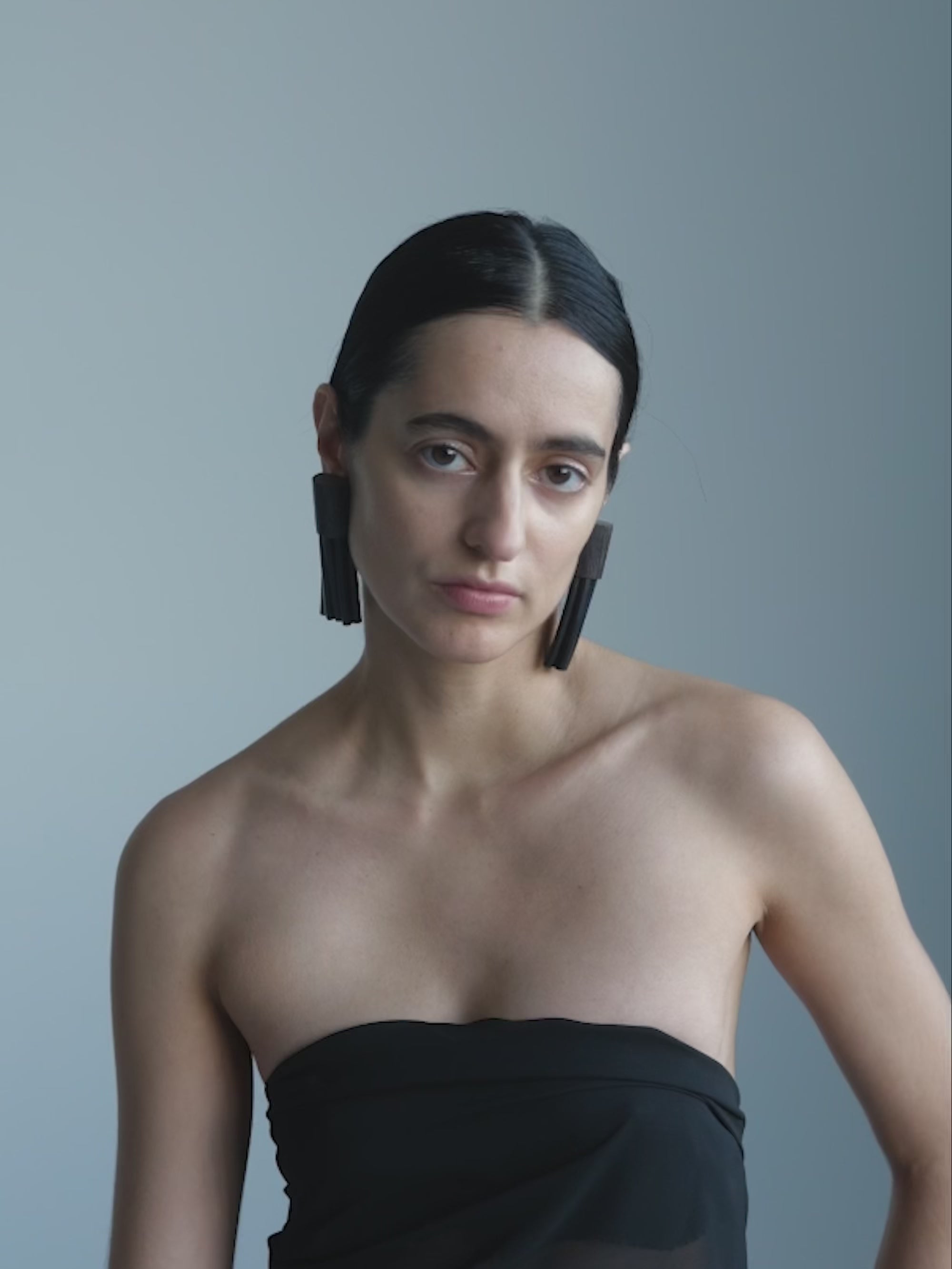 Woman wearing a black strapless top and tassel earrings against a gray background