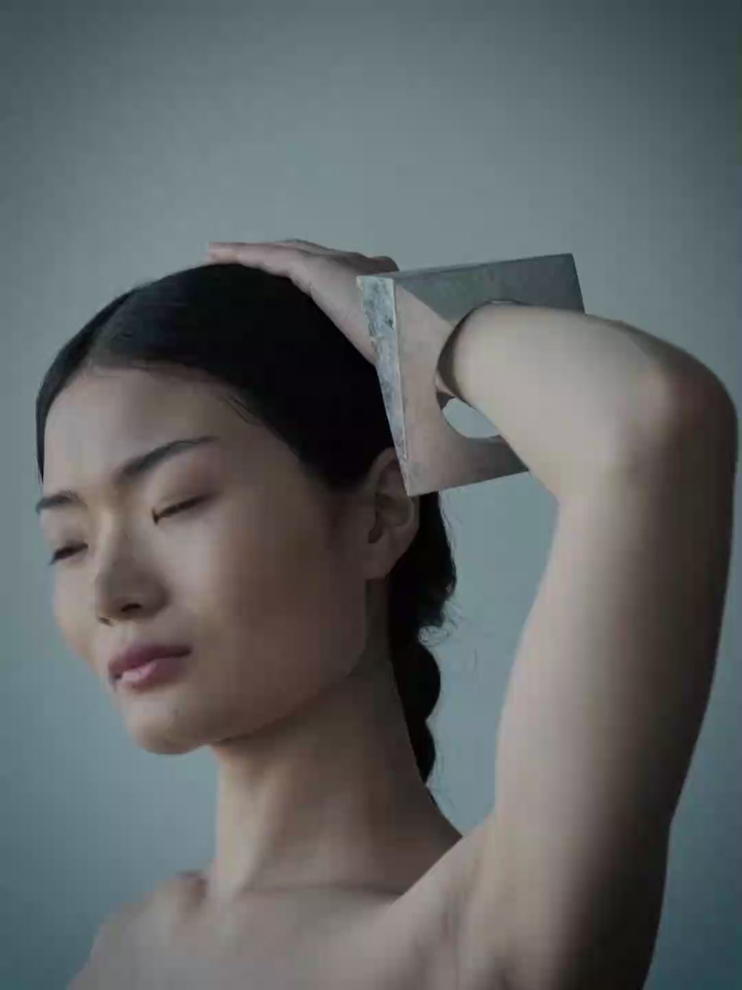A woman wearing a wide, chunky silver geometric cuff bracelet, posing with her arm raised against a cool blue-gray background.