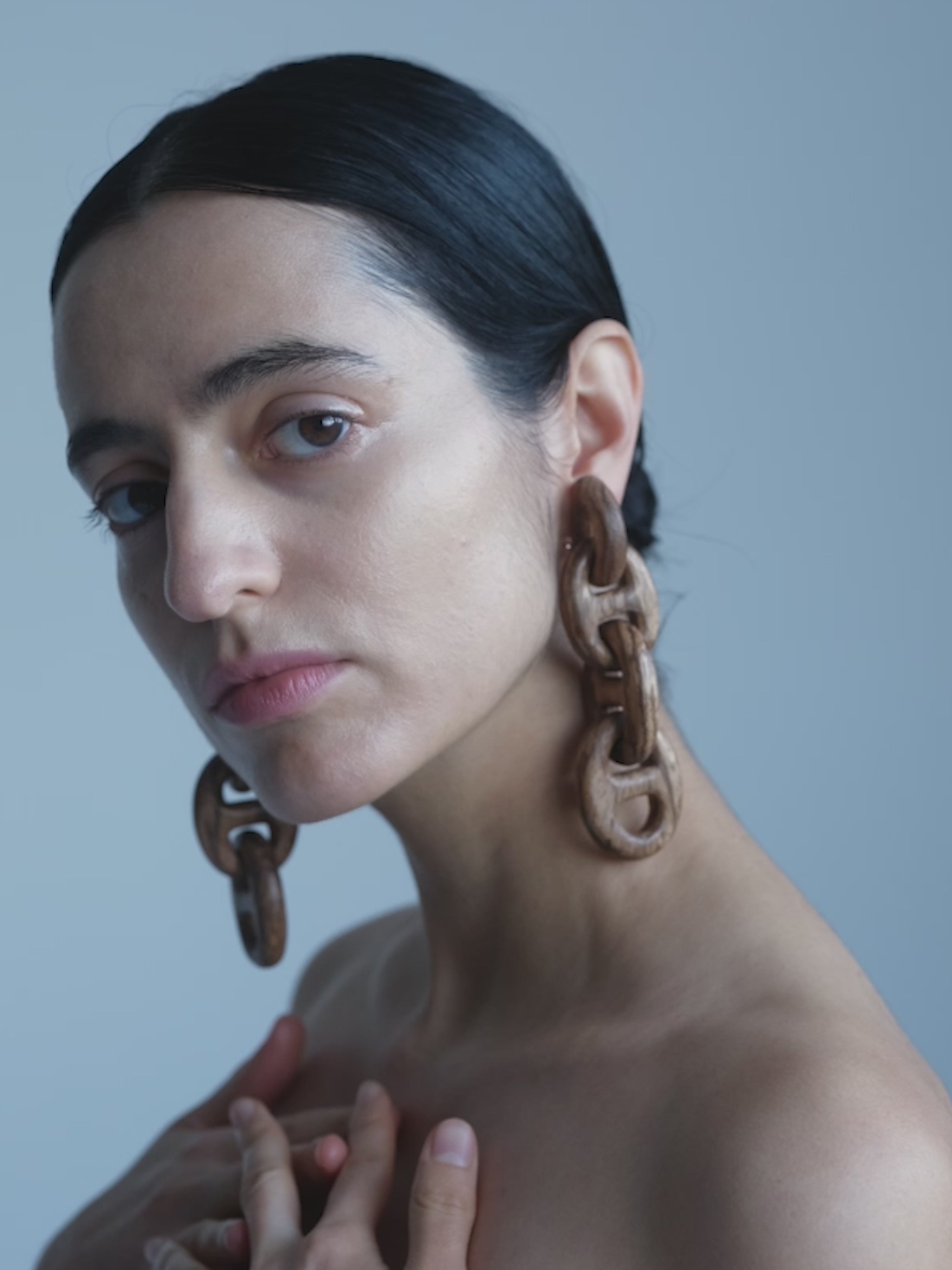 Woman wearing large chain earrings against a neutral background