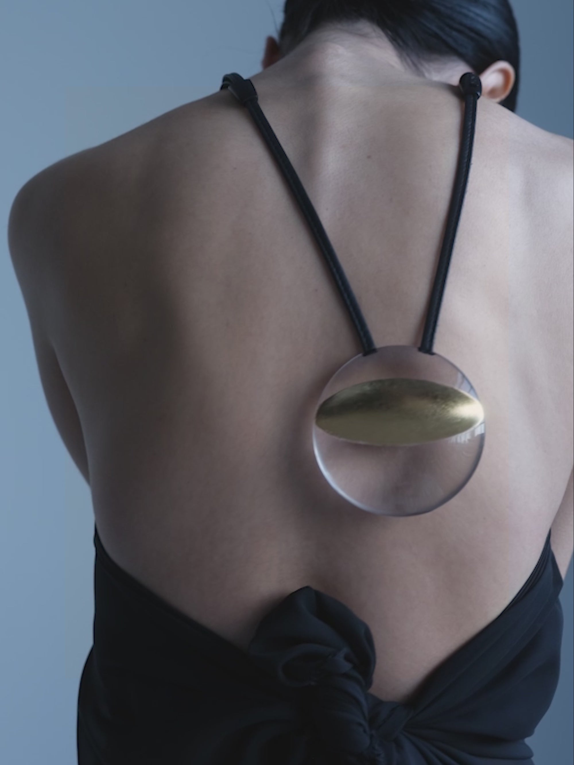 WOman wearing a black dress and a Necklace with a gold and transparent pendant on a black cord against a white background