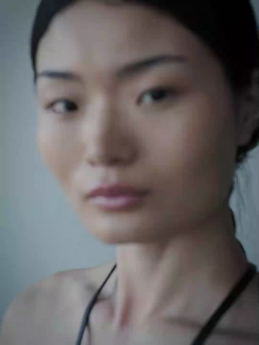 A woman viewed from behind wearing a dark wood geometric back ornament with black straps, set against a cool blue-gray background.