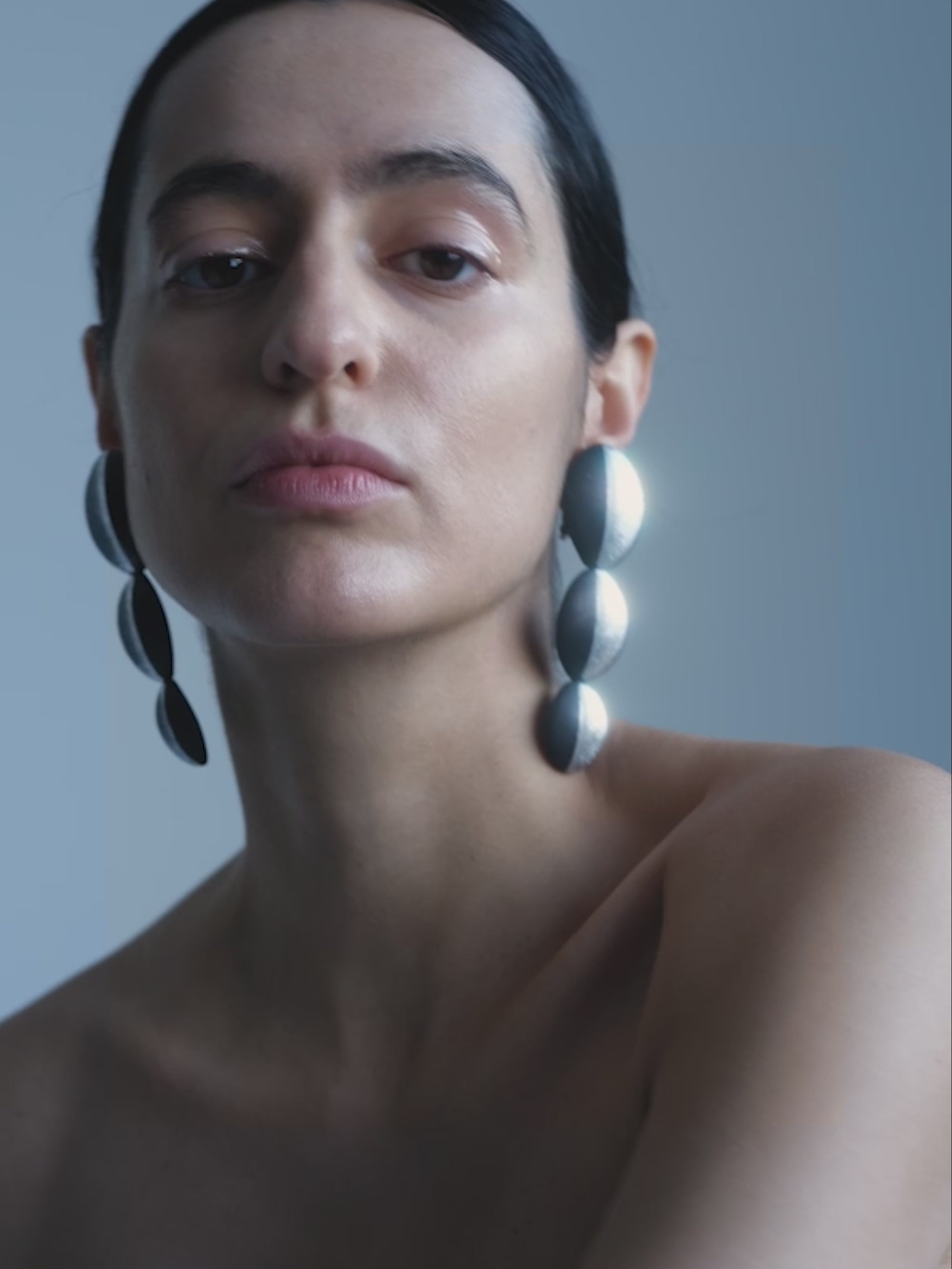 Woman wearing large, stylish earrings against a plain background