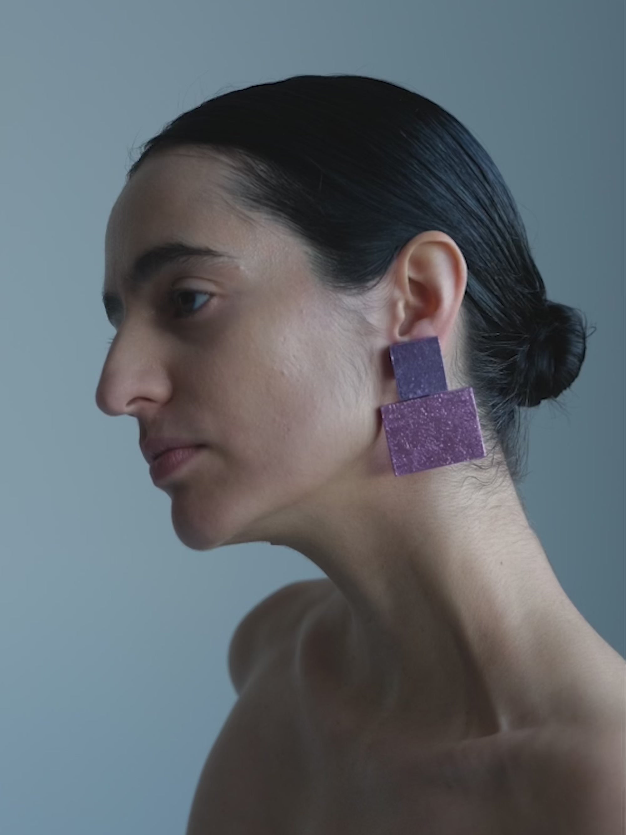 Woman wearing Pair of square-shaped earrings in pink and purple on a white background