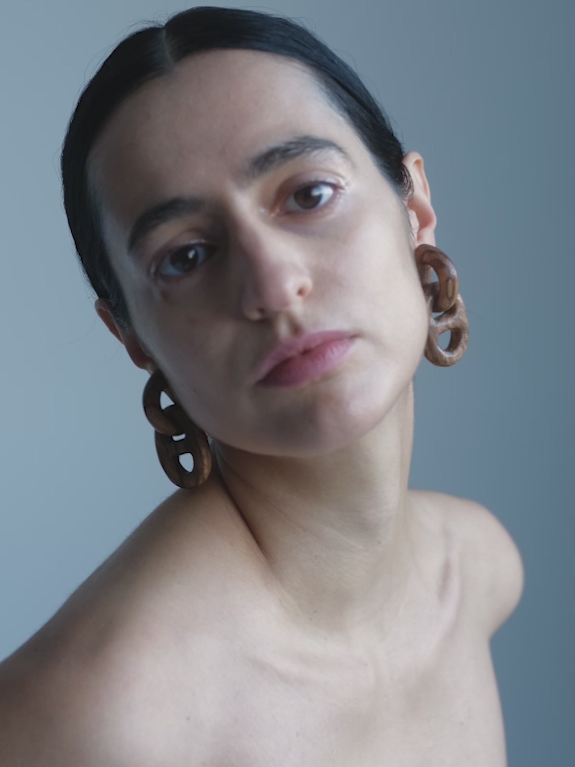 Woman with dark hair and earrings against a plain background