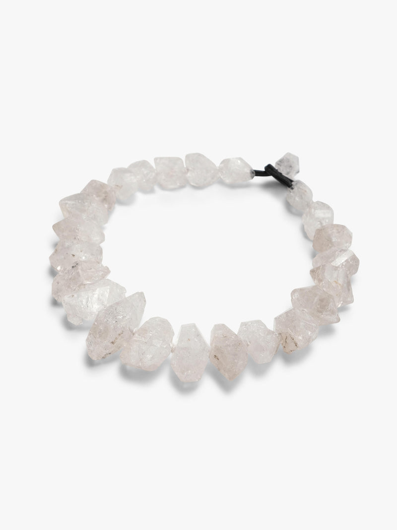 A beaded stretch necklace made of  white raw crystal chips, tied with a black elastic band, shown on a plain light gray background.