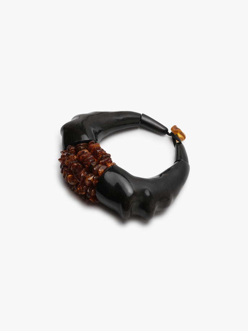 A chunky statement necklace featuring a glossy black horn frame with a textured cluster of amber-brown beads at the center and a small amber accent at the top clasp, shown on a plain light gray background.