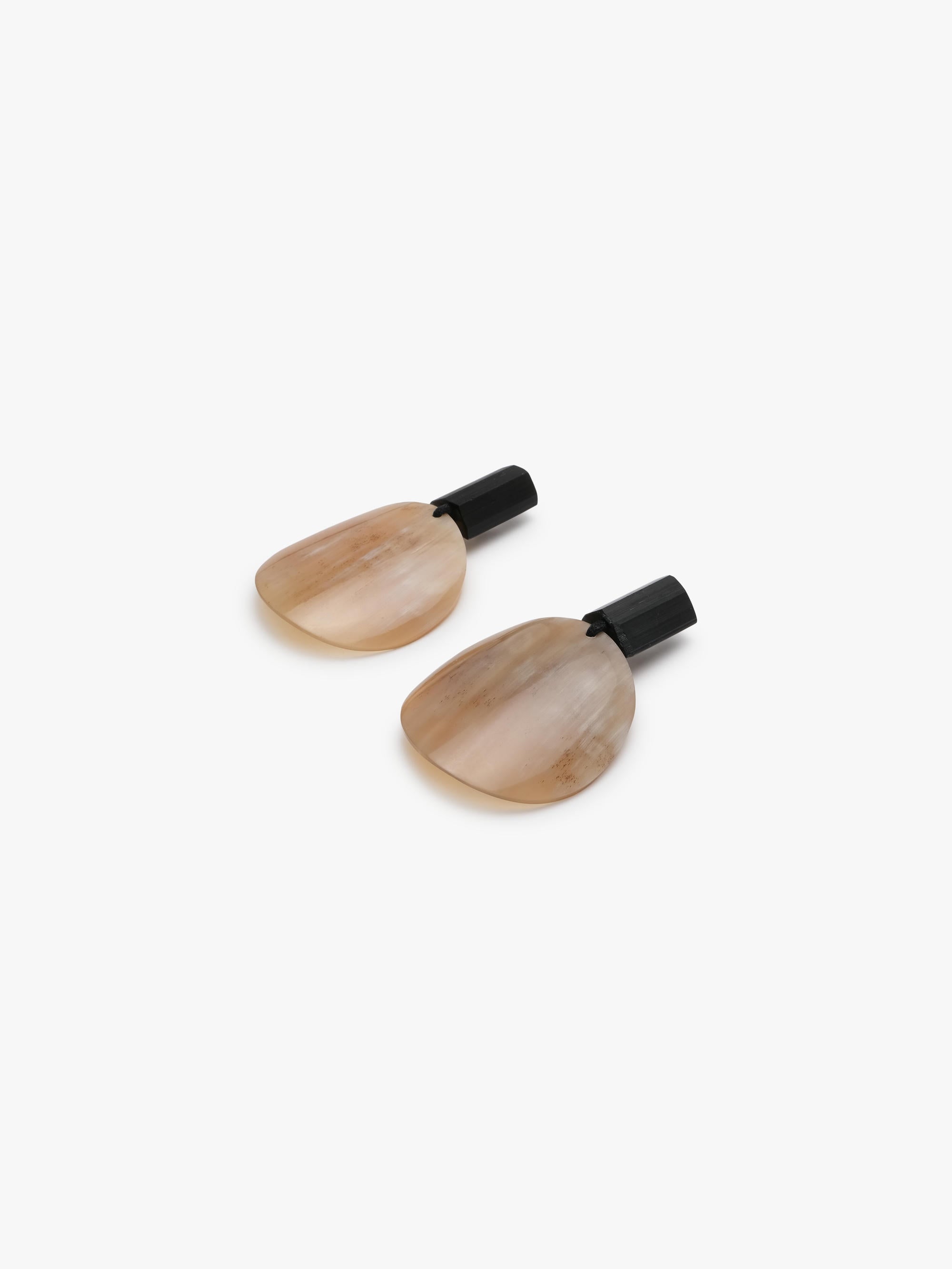 A pair of minimalist drop earrings featuring organic, teardrop-shaped beige and brown horn pendants with black stone posts, shown against a plain white background.